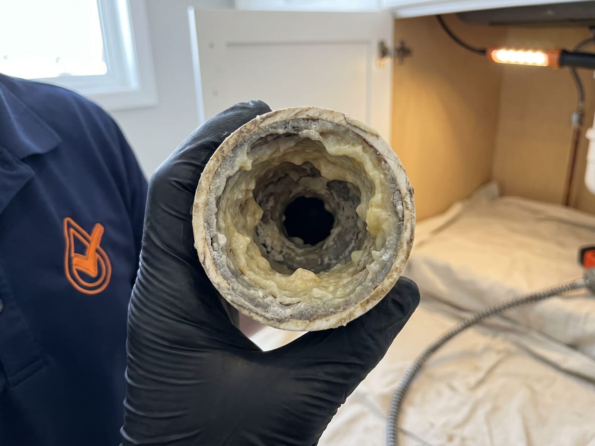 Cross-section of a kitchen pipe coated wall-to-wall with grease and hard-water scale, showing why a slow kitchen drain won't clear after snaking in Edmonton